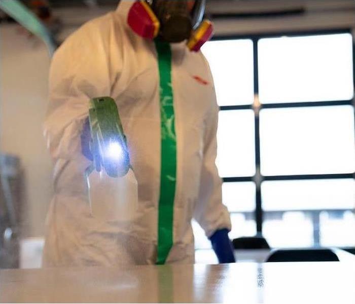 Someone in a white hazmat suit spraying a surface